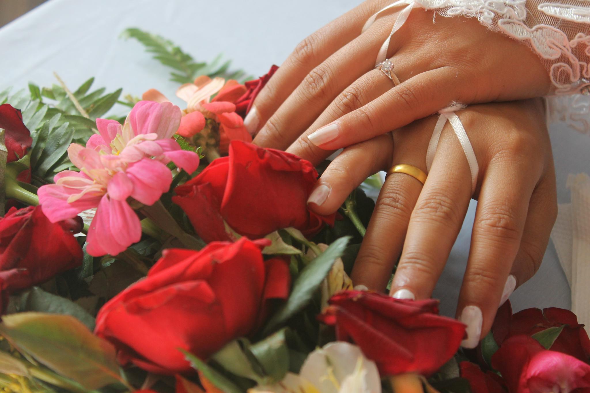 A bride and groom's hands elegantly placed over a vibrant bouquet of red roses, symbolizing love.