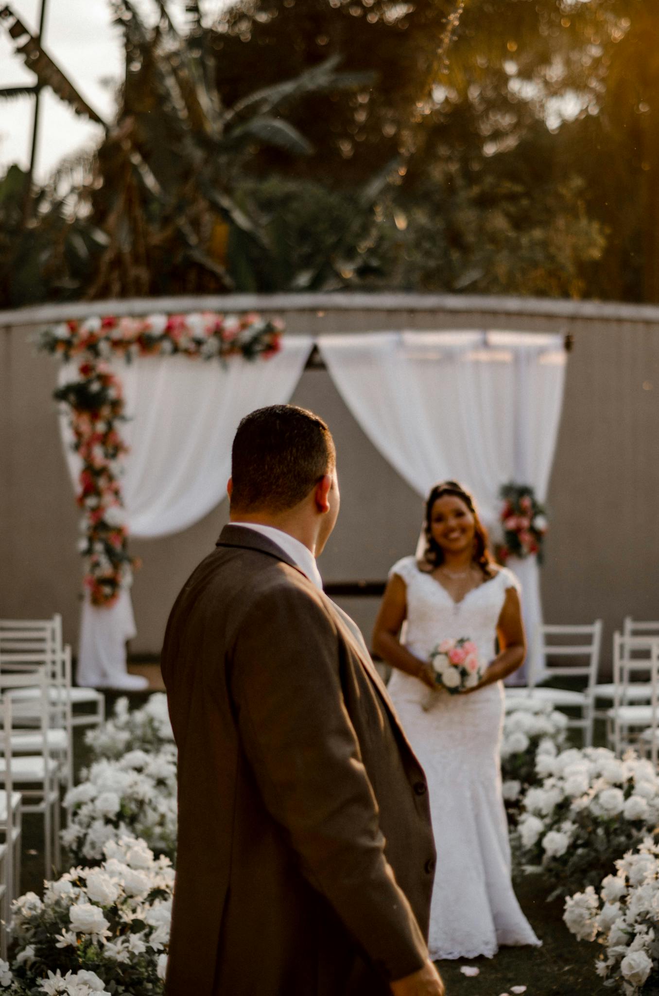 A couple celebrates their wedding in a romantic outdoor setting under sunset lighting with floral decor.