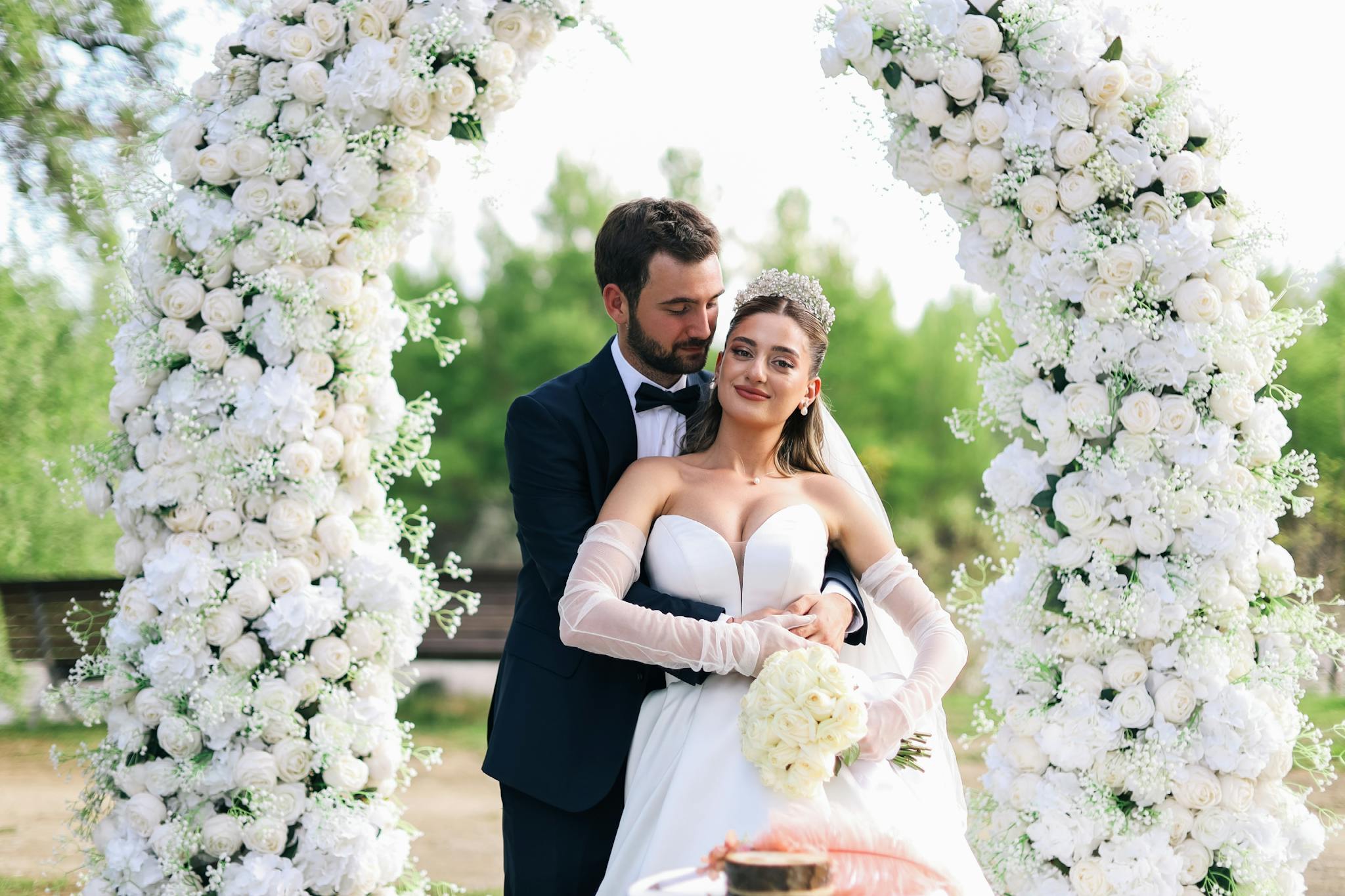 Beautiful outdoor wedding with a couple under a floral arch, captured in natural light.