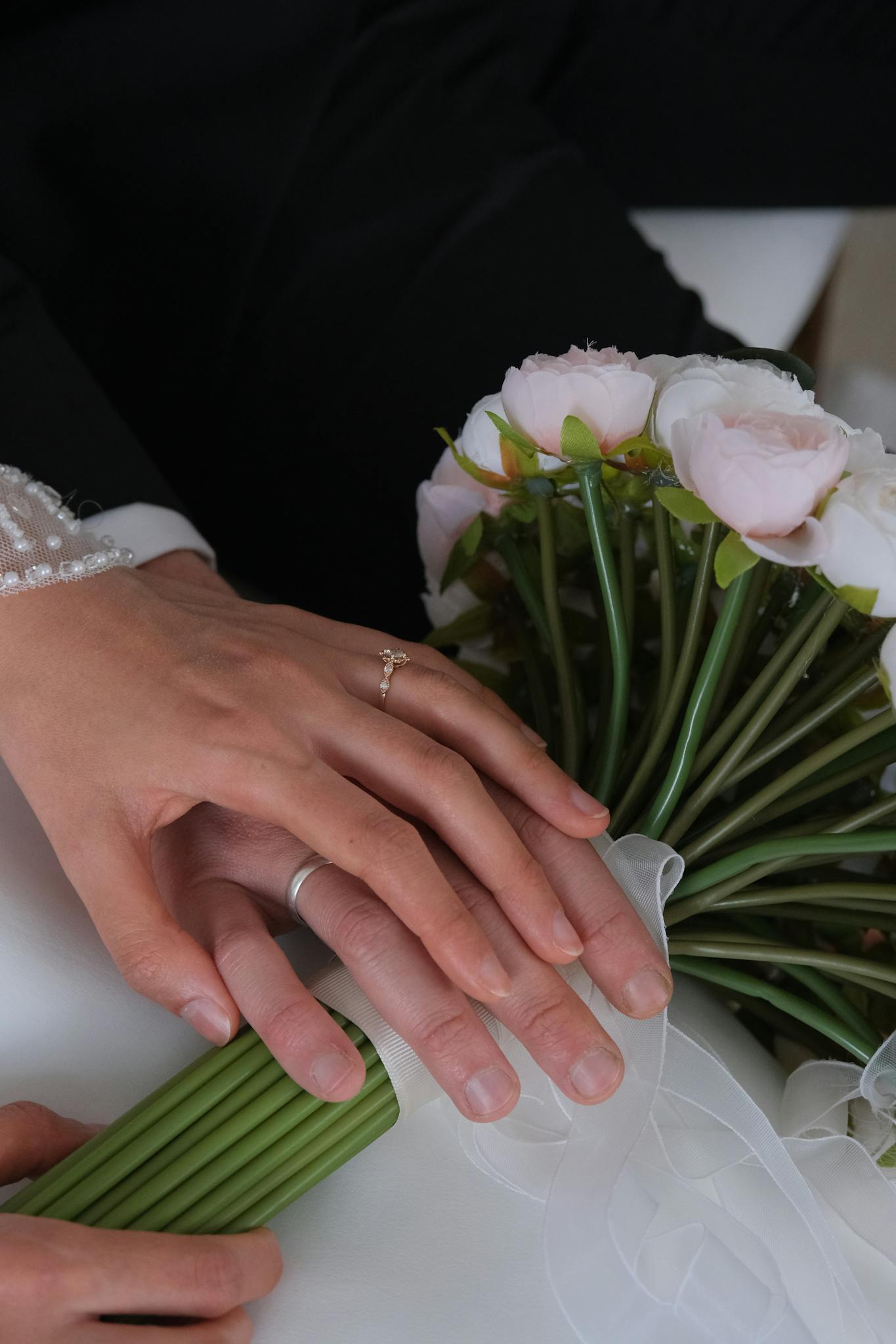 Close-up of couple's hands with wedding rings and rose bouquet, symbolizing love.