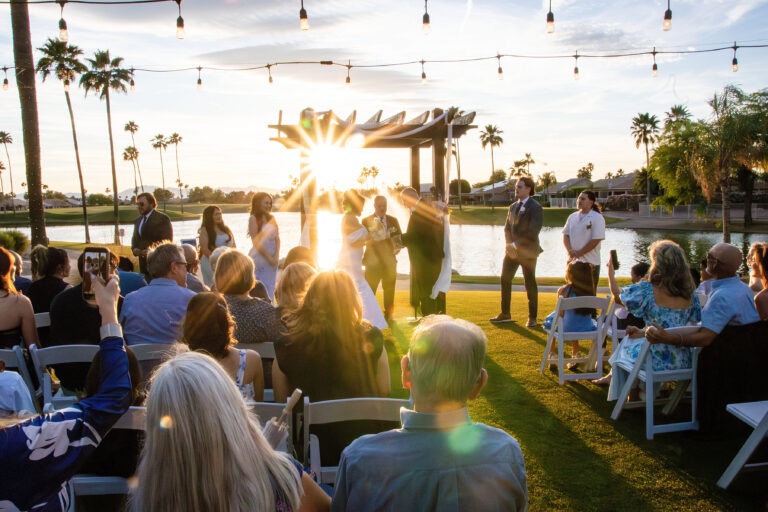 Sunset outdoor wedding ceremony in Arizona with guests gathered lakeside during golden hour photography by Sweet Owl Photography